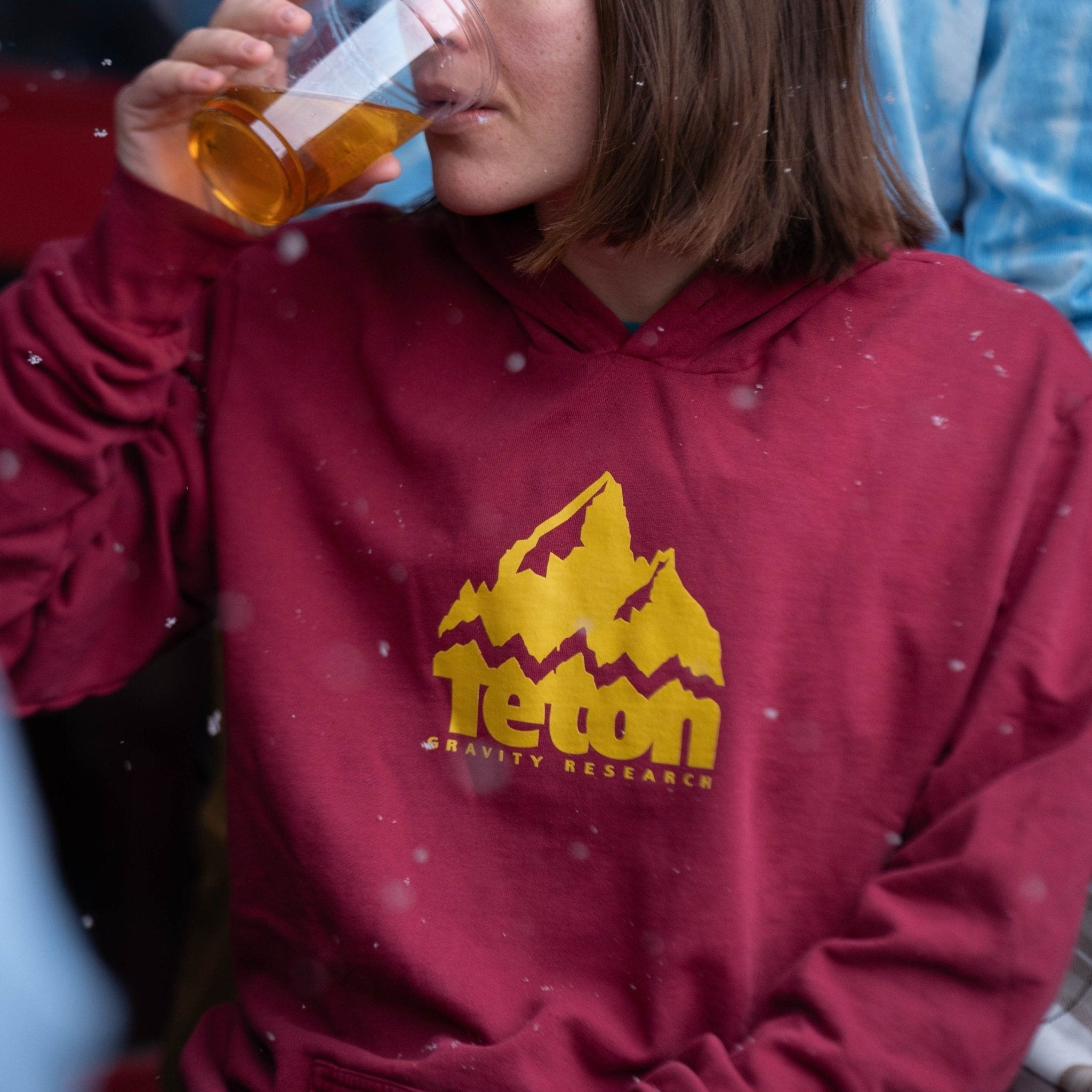 Showing a girl drinking a beer while wearing the Grang Logo Hoodie 2.0 in maroon