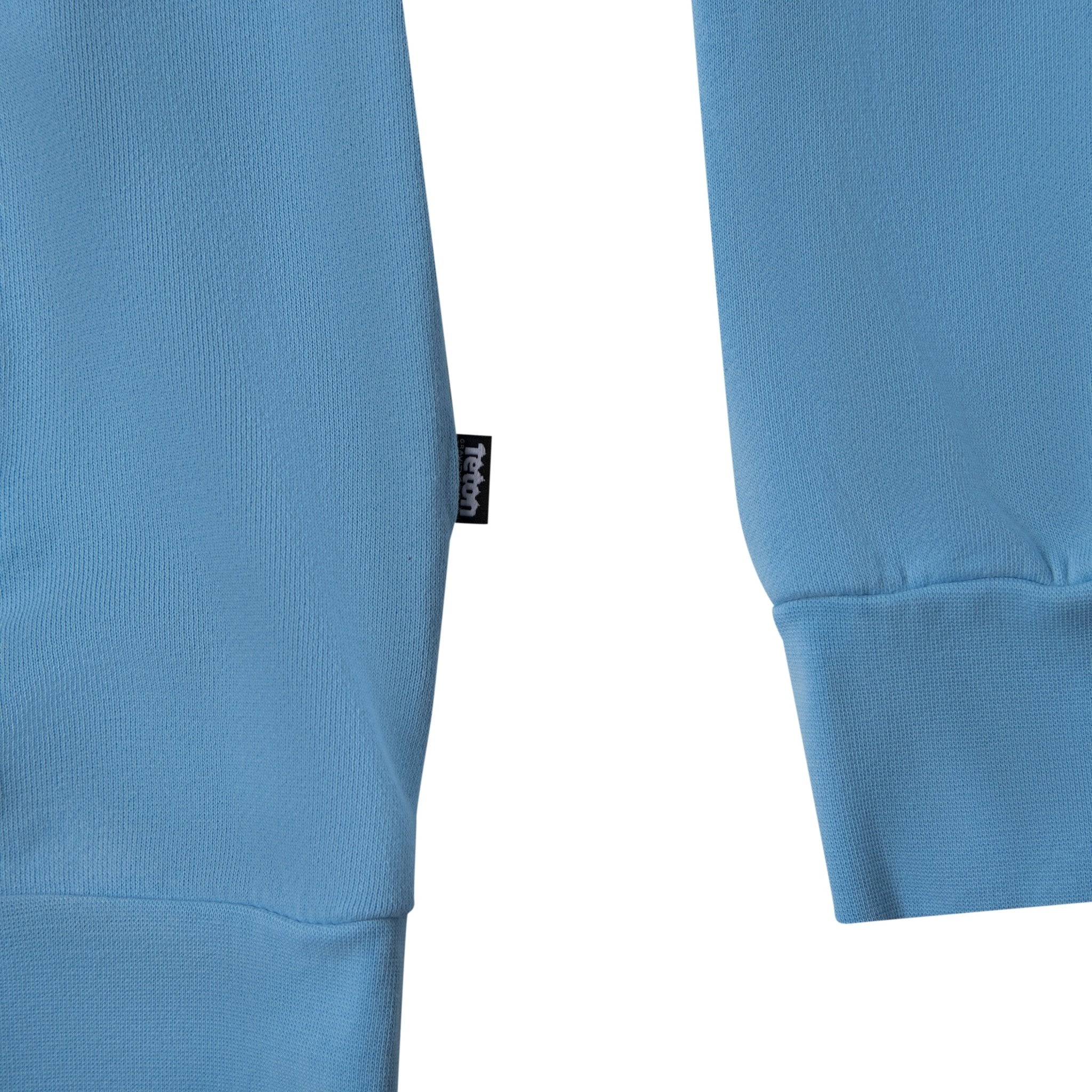 Picture of the small logo tag on the bottom left seam of the sweatshirt. #color_baby blue