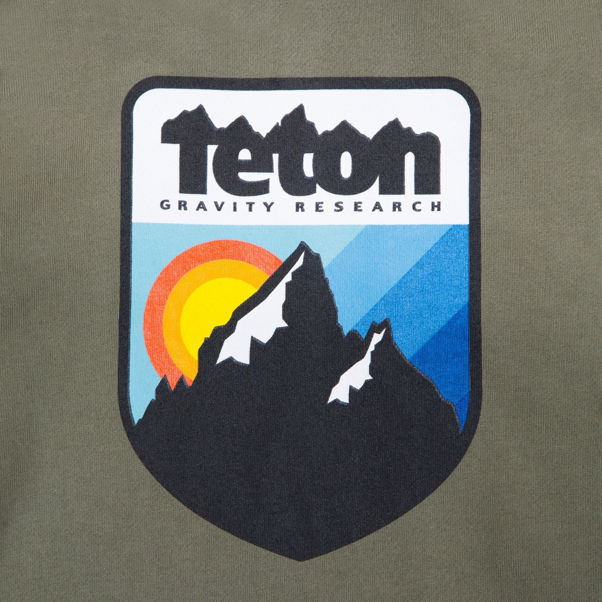Picture of the logo on the front of the sweatshirt. Shoes the Teton Gravity Research logo with the Grand Tetons and a sunset in the background. #color_Army Green